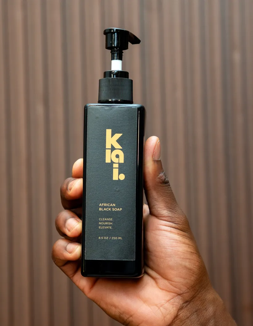 A hand holding the klai. bottle, label reading African Liquid Black Soap, cleanse nourish elevate, 8.5 oz / 250 ml